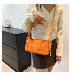 Detail of bright orange faux leather handbag with golden logo and detachable shoulder strap