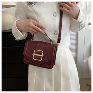 Detail of burgundy textured leather bag featuring a gold buckle and elegant strap