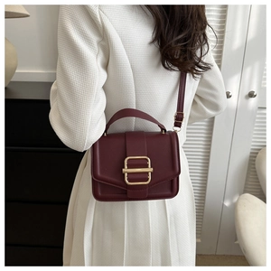 Detail of burgundy textured leather handbag with gold metal buckle on a white dress