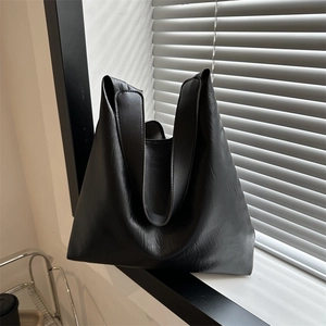 Minimalist large black tote bag in pebbled leather texture with elegant sunlight shadow
