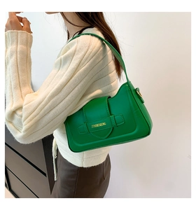 Detail view of a glossy green underarm bag with gold buckle and brand logo on model