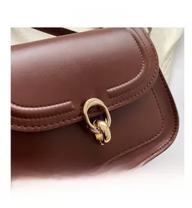 Détail de la texture en cuir marron et de la boucle en métal doré du sac à bandoulière