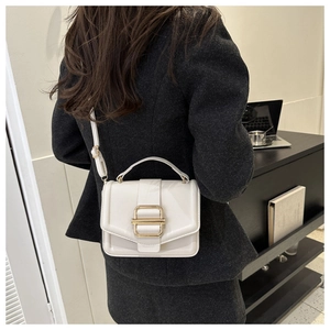 Detail of off-white crossbody bag with gold buckle hardware and pebble grain texture
