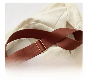 Détail d'une large bandoulière en tissu marron foncé avec boucle métallique dorée