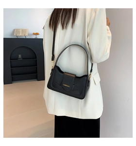 Model wearing black leather shoulder bag with gold lettering and metallic hardware details