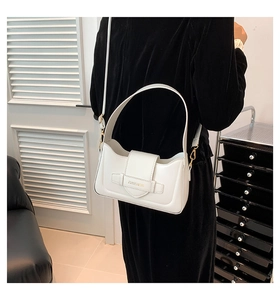 White minimalist shoulder bag with gold hardware and logo detail worn by a model