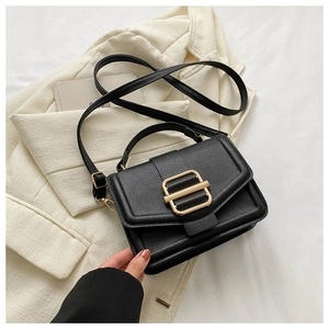 Detail of black lychee-textured square handbag with a large gold metal buckle on white fabric