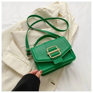 Detail of green textured leather handbag with gold metal buckle on a white blazer