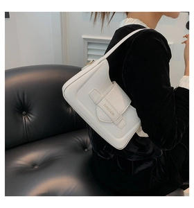 Detail of a white leather underarm bag with gold logo and magnetic closure on a model