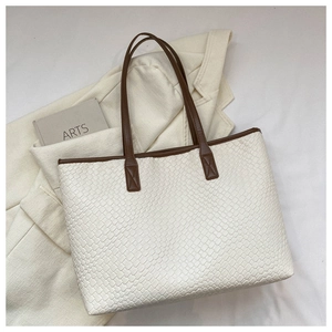 Vue détaillée du cabas blanc tressé avec poignées marron sur fond de veste chic