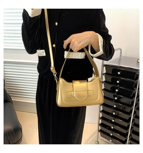 Detail of a metallic gold shoulder bag with adjustable strap on a velvet outfit