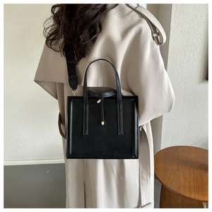 Détail d'un sac à main carré noir minimaliste porté avec un trench-coat beige sur l'épaule