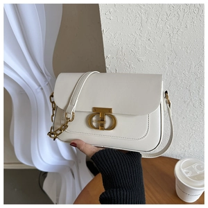 Détail du sac bandoulière blanc avec boucle dorée et chaîne sur une surface en bois