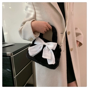 Détail du sac à main en peluche noire avec nœud en satin blanc et bandoulière en perles