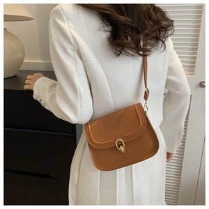 Gros plan d'un sac bandoulière en cuir marron avec surpiqûres en U et boucle dorée