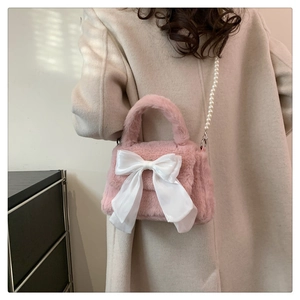 Vue détaillée du sac en peluche rose avec un grand nœud blanc et une sangle en perles