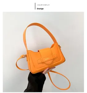 Detailed view of the vibrant orange leather underarm bag with decorative brand strap