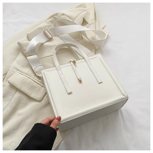 Détail d'un cabas blanc en cuir avec une large bandoulière en tissu et un fermoir boule doré