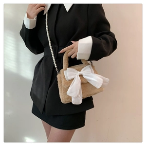 Dettaglio borsa di peluche con fiocco bianco e tracolla di perle su blazer nero