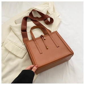 Détail d'un sac cabas marron en similicuir avec large bandoulière sur un blazer