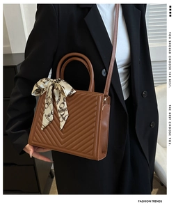 Brown quilted crossbody bag with decorative silk scarf on handle and sleek V-shaped stitching