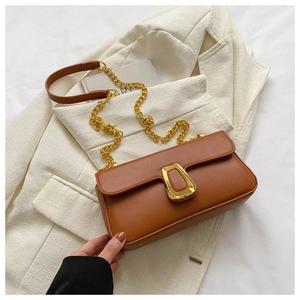 Detail of a brown leather bag with a gold metal buckle and chunky chain strap on a white blazer