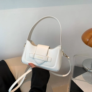 Minimalist white designer shoulder bag with flap closure and dual straps in a home setting