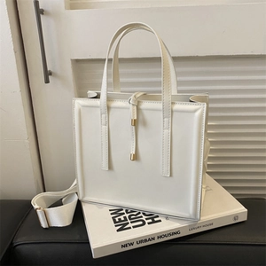 Sac cabas carré blanc crème minimaliste avec large bandoulière posé sur un livre
