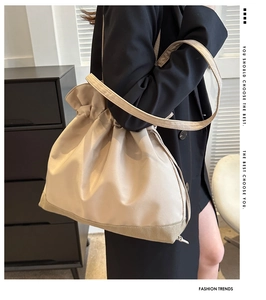 On-shoulder view of a beige drawstring hobo bag with contrast stitching and nylon finish