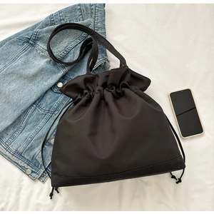 Detail of black drawstring bucket bag with stitching on white textured fabric