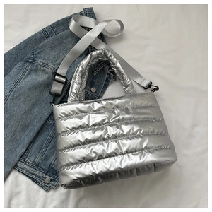 Silver metallic quilted puffer handbag with adjustable woven strap on denim background