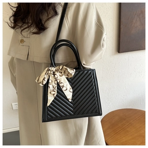 Détail du sac noir avec matelassage en V et foulard en soie imprimé rétro sur la poignée