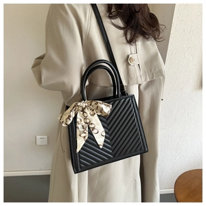 Detail of black quilted leather handbag with chic silk scarf on the top handle and long strap