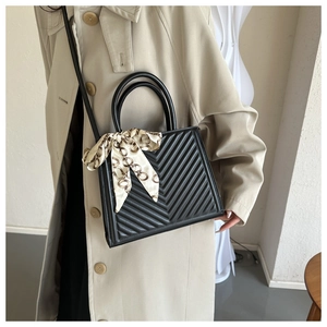 Détail d'un sac à main noir matelassé en V avec foulard en soie et bandoulière