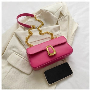 Detail of a bright pink leather shoulder bag with a large golden metal clasp and chain