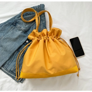 Detailed top view of a minimalist yellow drawstring tote bag on a casual fabric background