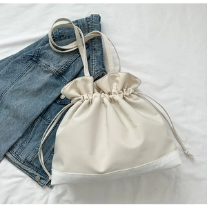 Detail of minimalist drawstring handbag in soft cream leather on a casual denim background