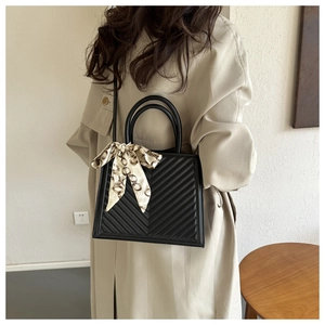 Close-up of black quilted leather handbag with decorative chain-print silk scarf handle