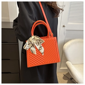 Detail of bright orange quilted PU leather handbag with decorative silk scarf and strap
