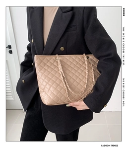 Dettaglio borsa tote in pelle trapuntata beige con catena dorata su modella in completo