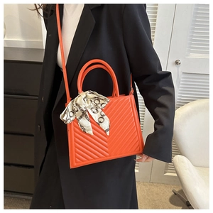 Orange quilted handbag with V-shaped stitching and silk scarf on a black suit outfit