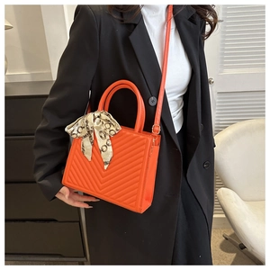 Vue détaillée du sac à main orange matelassé en V avec foulard en soie sur la poignée