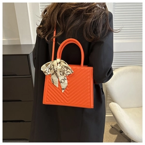 Détail du sac à main en cuir orange avec texture matelassée en V et foulard en soie