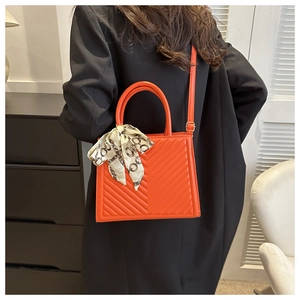 Détail du sac à main matelassé orange avec foulard à motifs chic sur la poignée