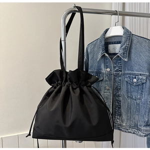 Detail of black nylon drawstring bucket bag showing pleated closure and shoulder strap