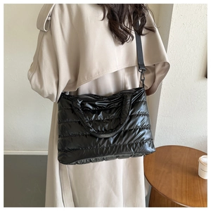 Model wearing a black glossy quilted shoulder bag with polished waterproof finish