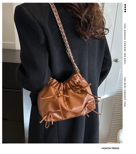 Detail of caramel pleated cloud bag with bow accent and metal chain shoulder strap