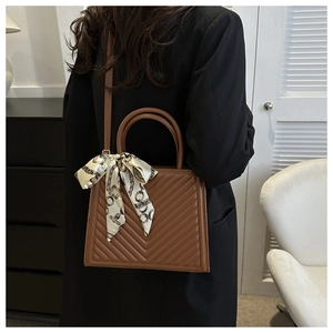 Sac à main marron avec matelassage en V, détail foulard en soie et poignées rondes sur modèle