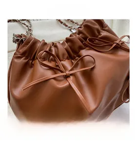 Detail of a brown pleated cloud bag with a decorative bow and silver chain strap