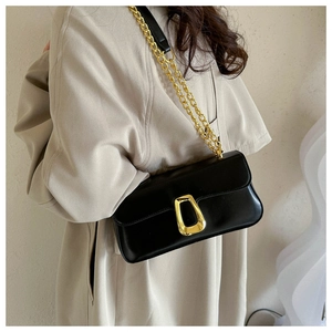 Detail of a minimalist black leather crossbody bag with a gold metal chain and buckle